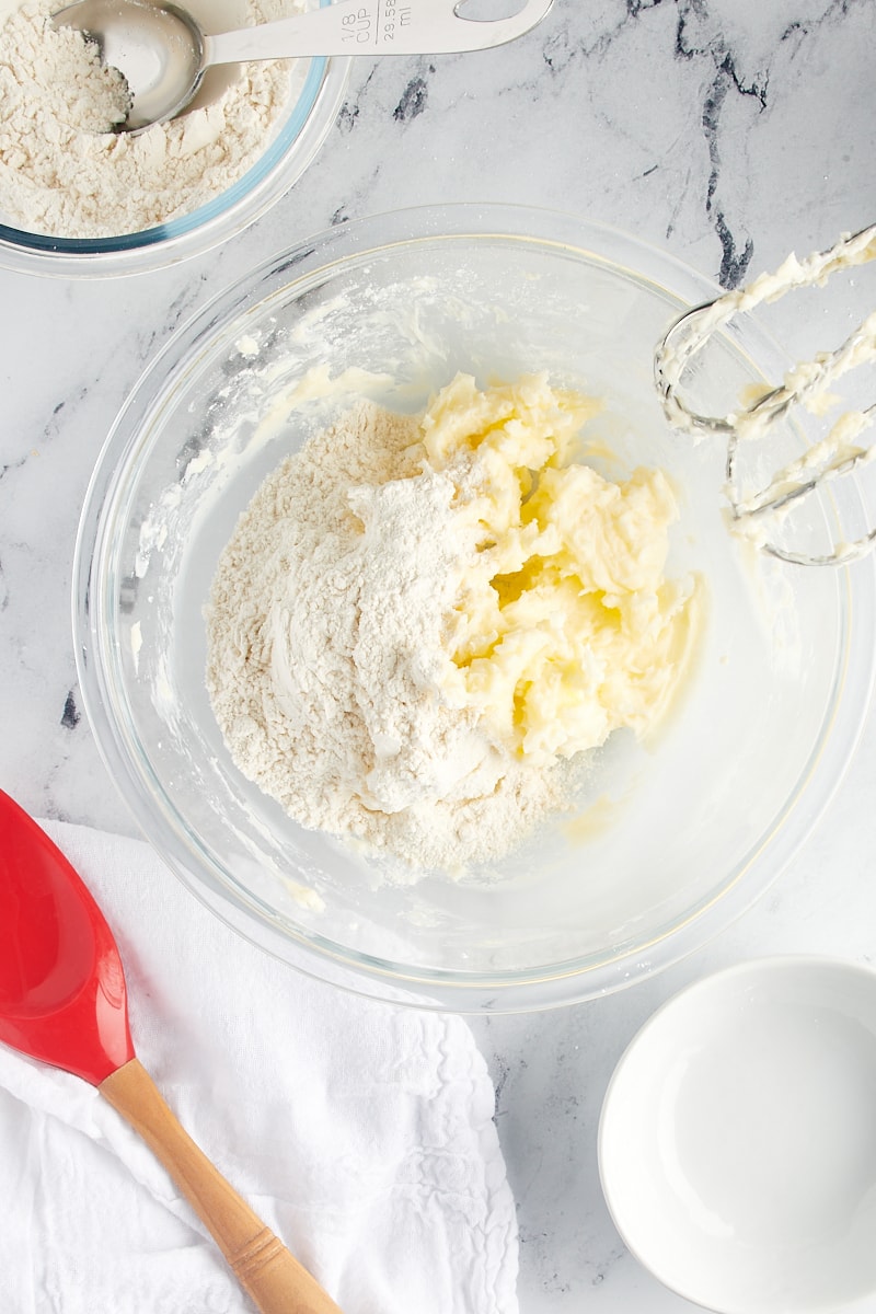 Overhead view of flour added to creamed butter and sugar in a glass mixing bowl.