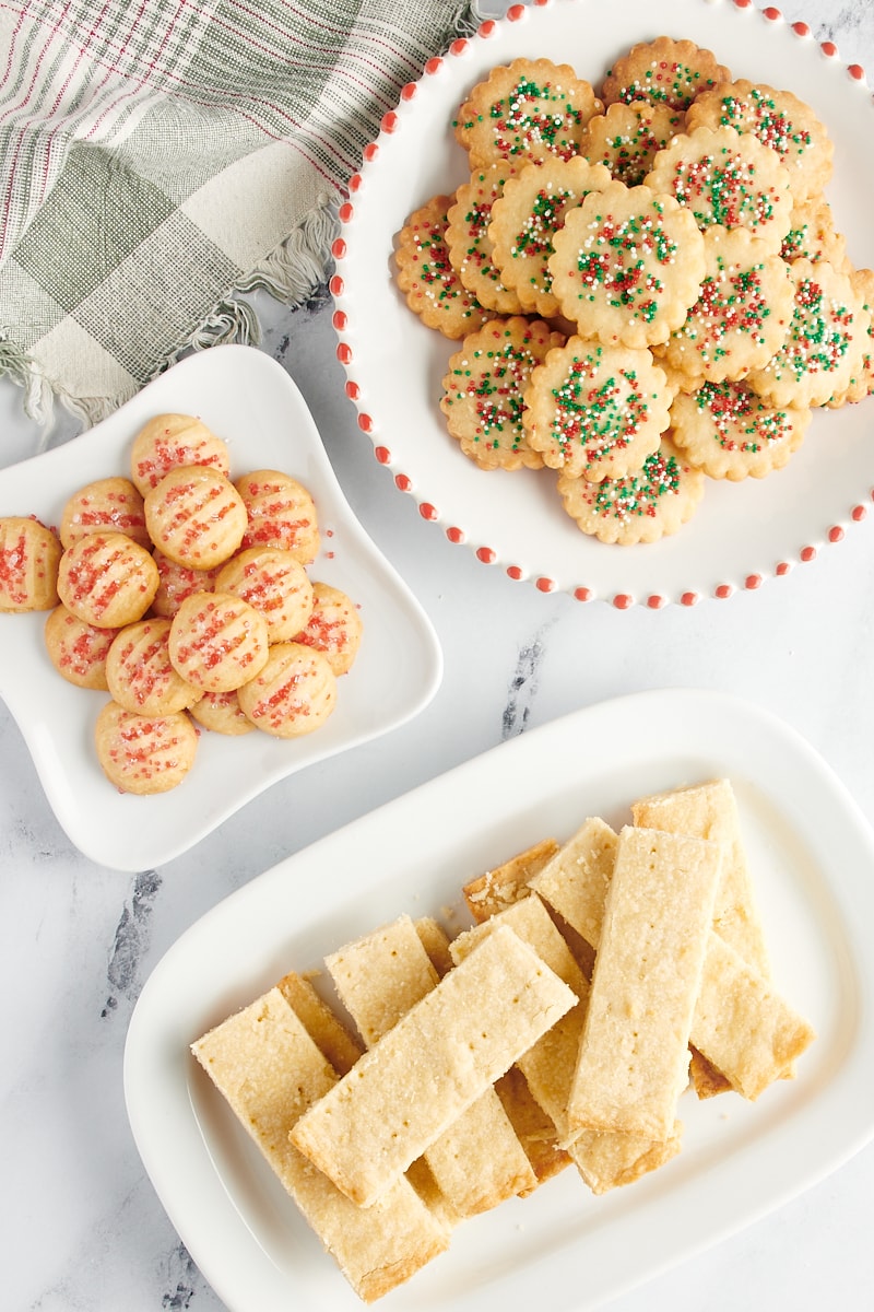 Overhead view of shortbread cookies in three different styles on white plates.