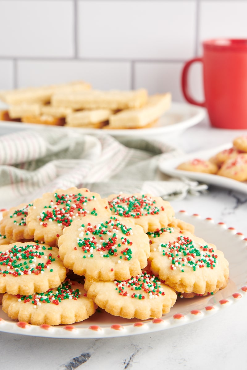 Shortbread cookies on a red-rimmed white plate with more cookies on plates in the background.