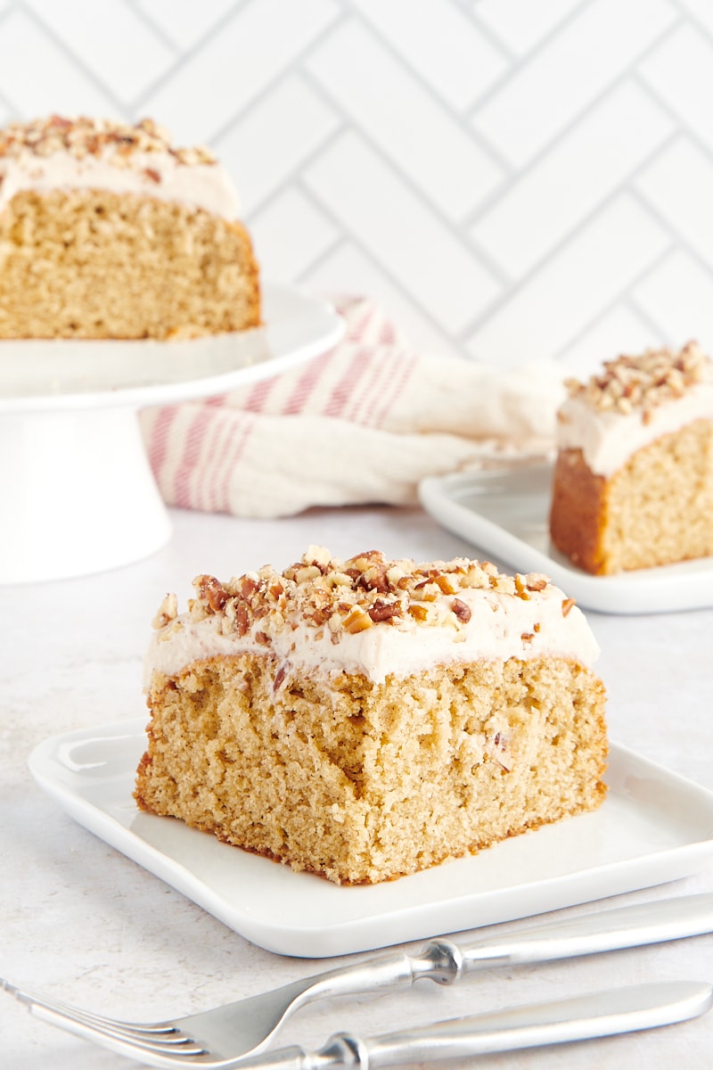 slice of Spice Cake on a white plate with more cake in the background