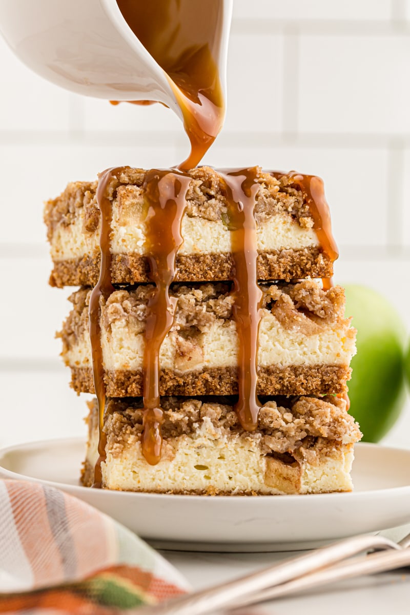 caramel sauce pouring over a stack of three Caramel Apple Cheesecake Bars