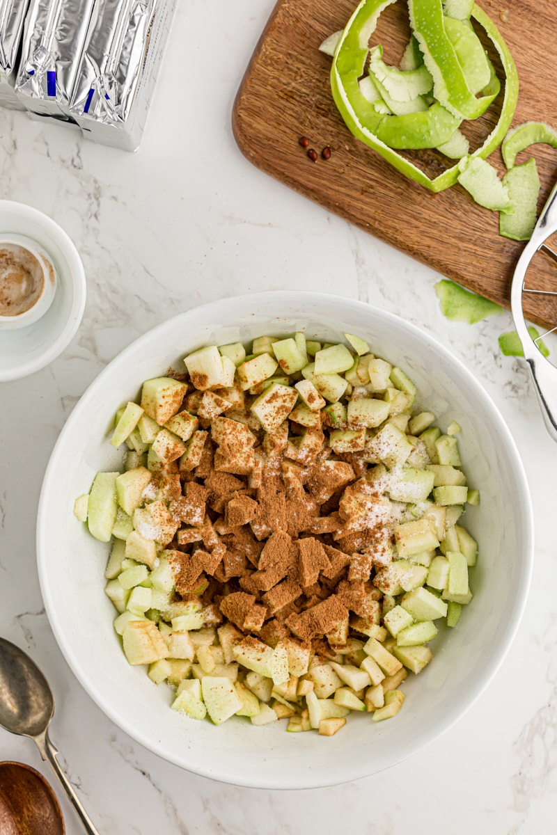 overhead view of diced apples, sugar, and cinnamon in a white mixing bowl