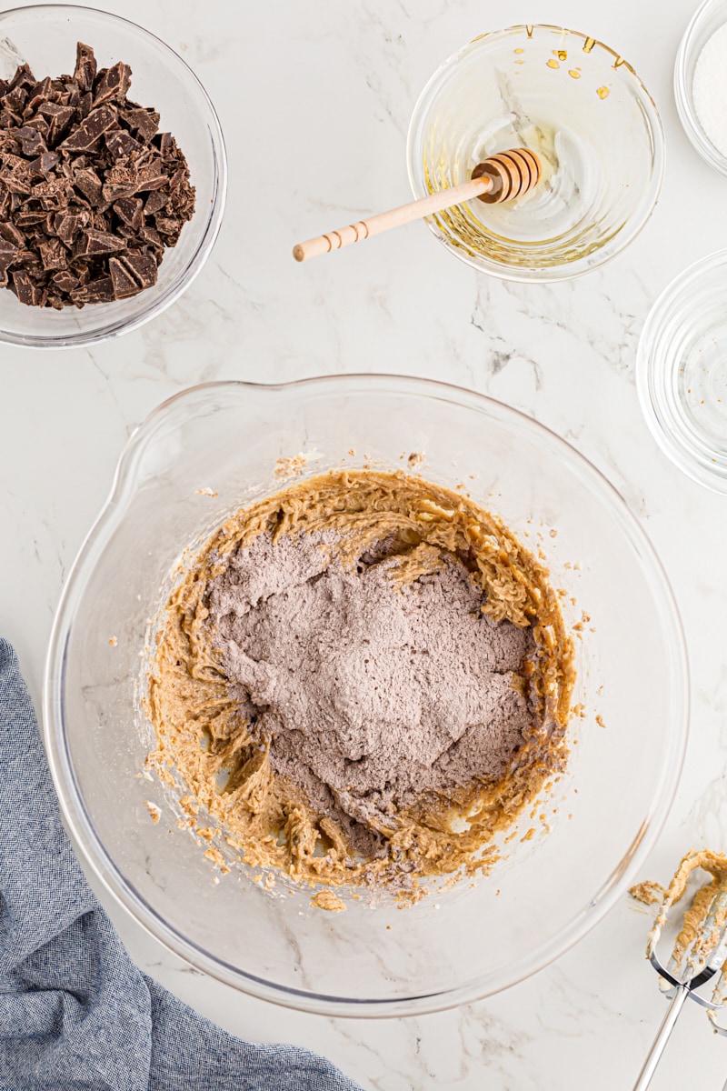 Overhead view of dry ingredients added to bowl of wet cookie ingredients