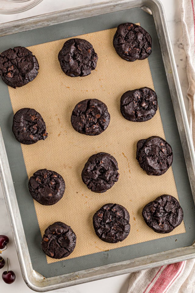 Overhead view of dark chocolate cherry cookies on a baking sheet.