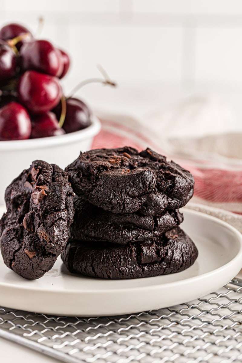 Stack of Double Dark Chocolate Cherry Cookies on plate with bowl of cherries in background