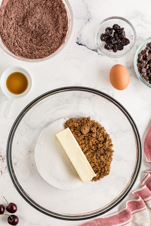 Overhead view of butter, brown sugar, and sugar in a glass mixing bowl.