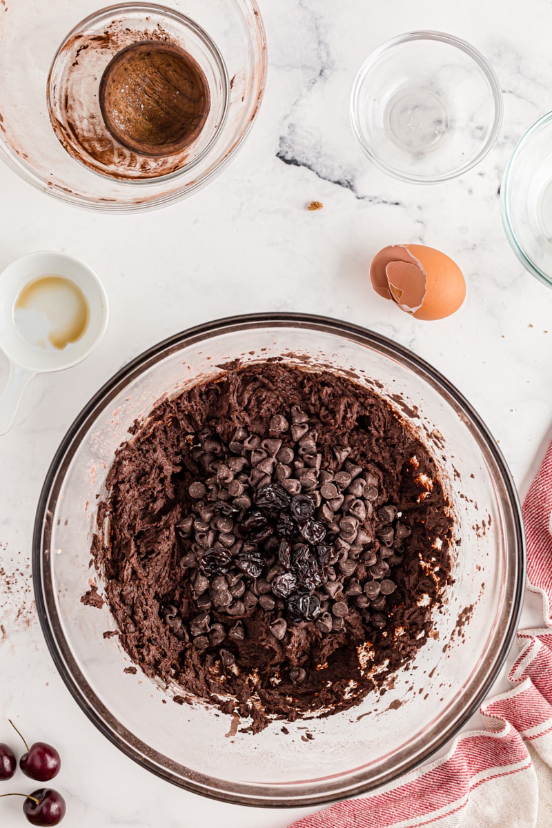 Adding chocolate chips and cherries to bowl of chocolate cookie dough