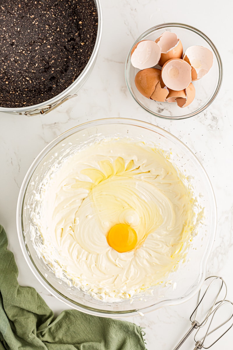 Overhead view of egg cracked into bowl of whipped cream cheese
