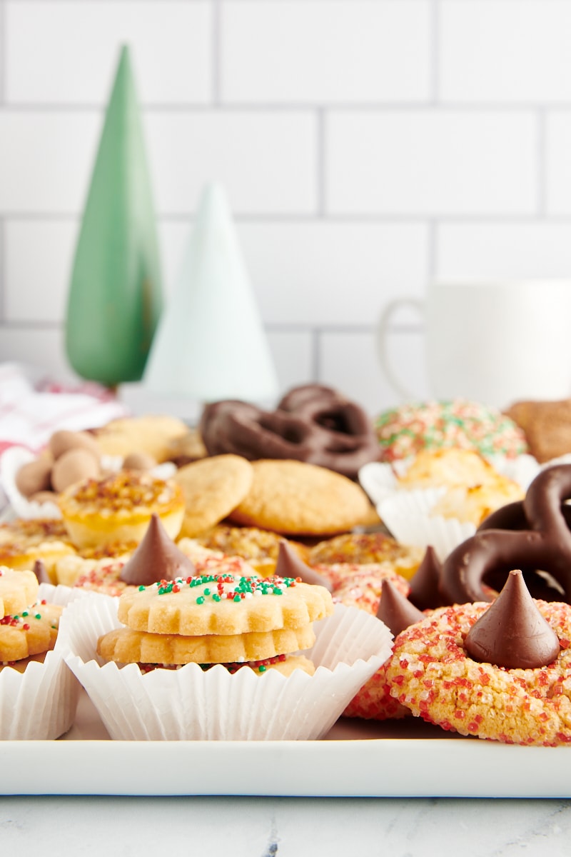 a serving tray filled with Christmas cookies with small wooden Christmas trees in the background