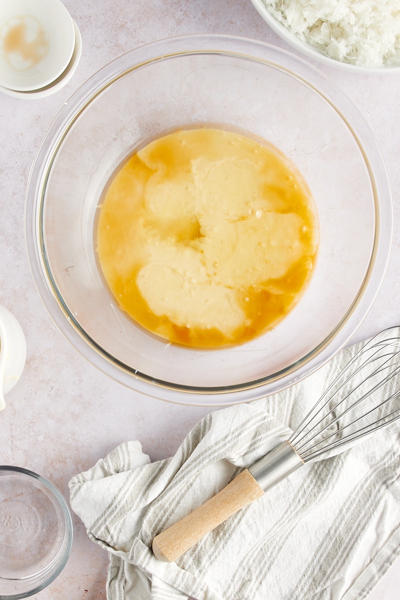 overhead view of sweetened condensed milk, egg white, vanilla extract, almond extract, and salt in a glass mixing bowl