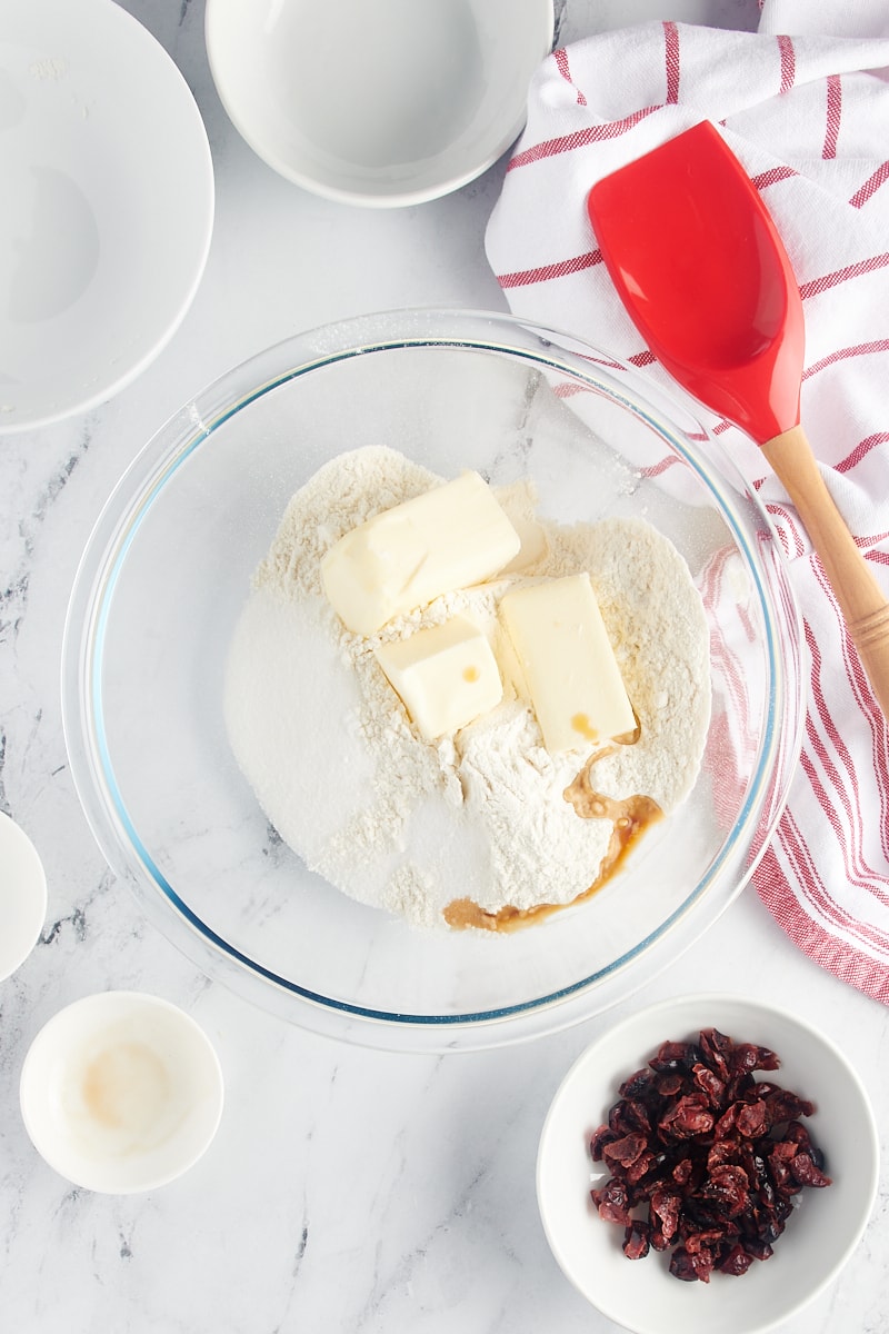 Overhead view of flour, butter, sugar, salt, and vanilla extract in a glass mixing bowl.