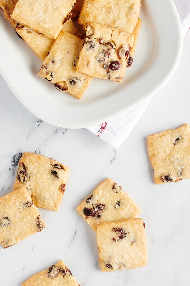 Overhead view of cranberry shortbread cookies scattered on a marble countertop and on a large white plate.