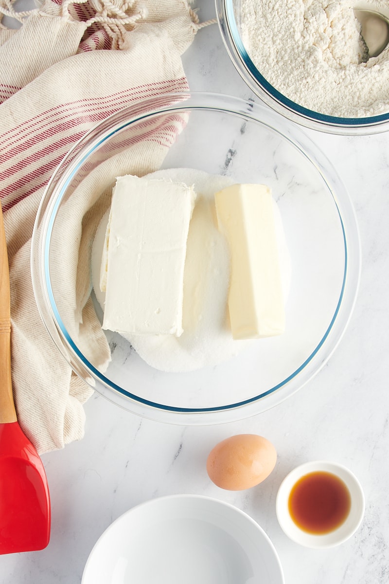 Overhead view of butter, cream cheese, and sugar in a glass mixing bowl.