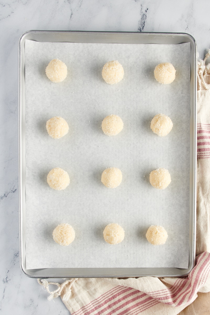 Overhead view of sugar cookie dough balls rolled in sugar and placed on a parchment-lined baking sheet.