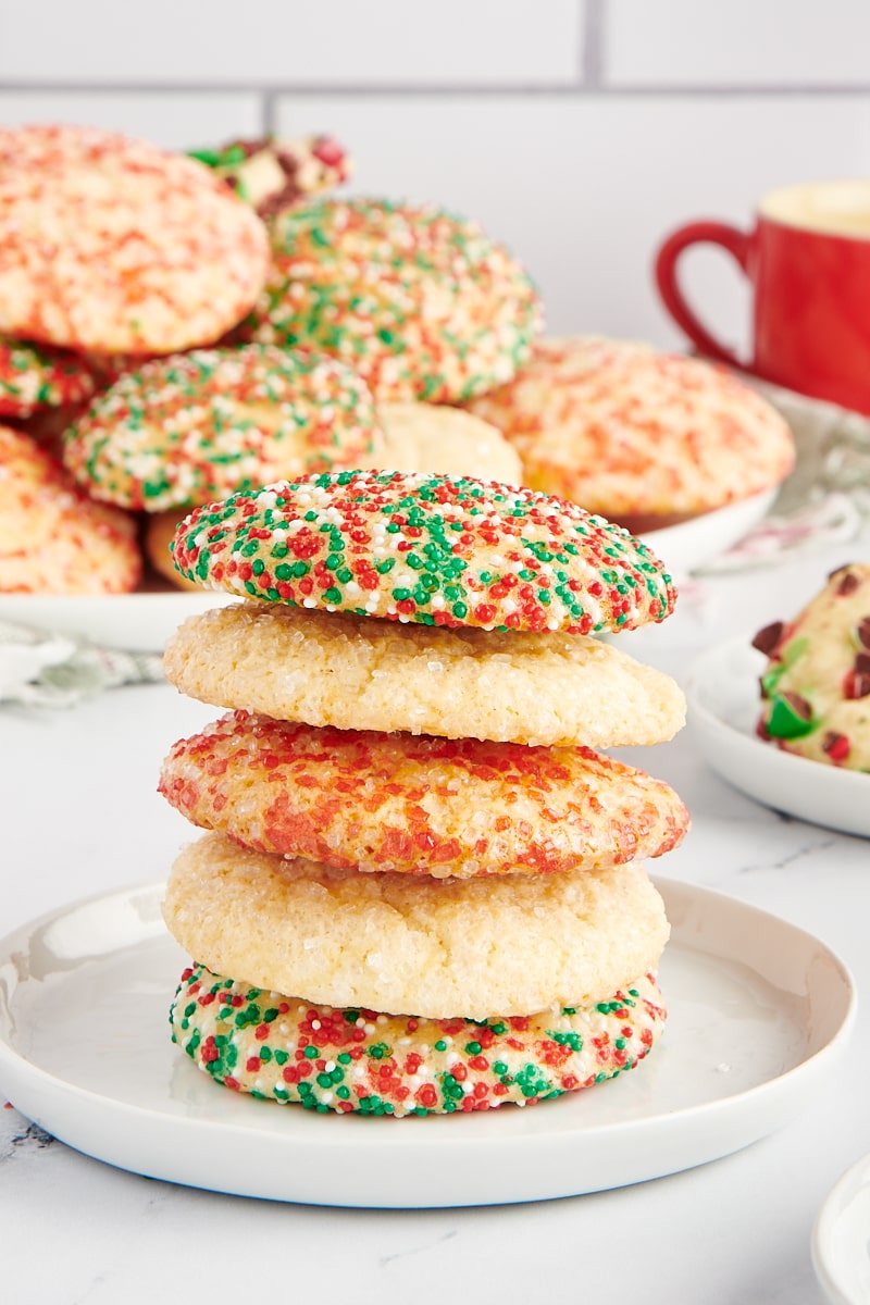 stack of sugar cookies on a small white plate with more cookies in the background