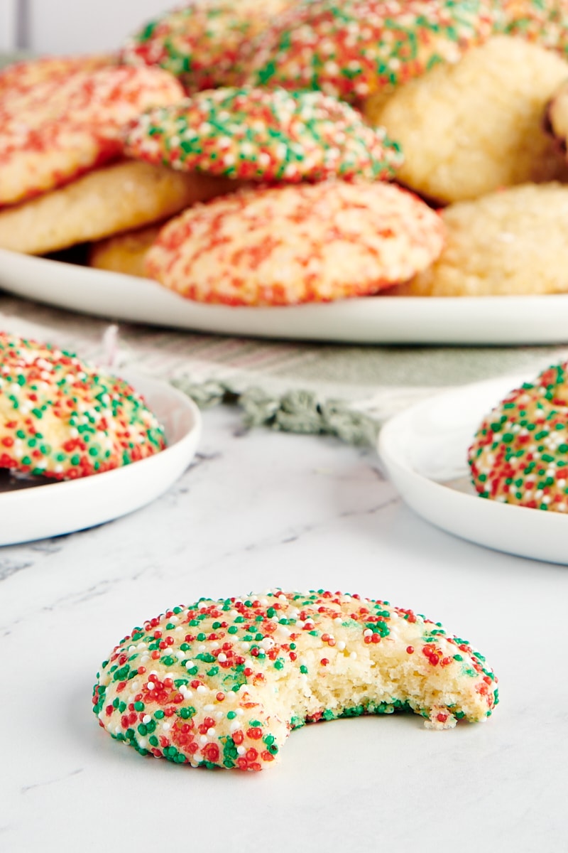 A sugar cookie with a bite missing and with more cookies in the background.