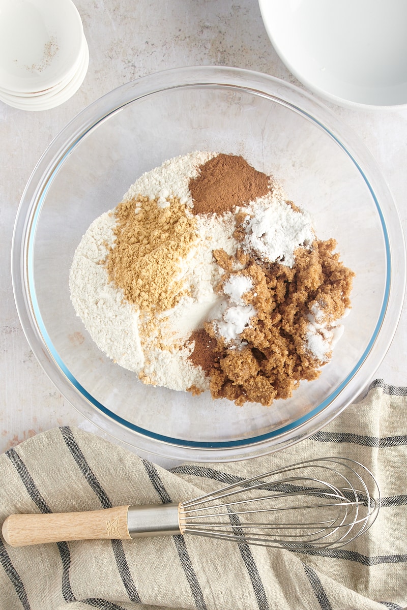 overhead view of flour, brown sugar, baking powder, baking soda, ginger, cinnamon, nutmeg, and salt in a glass mixing bowl