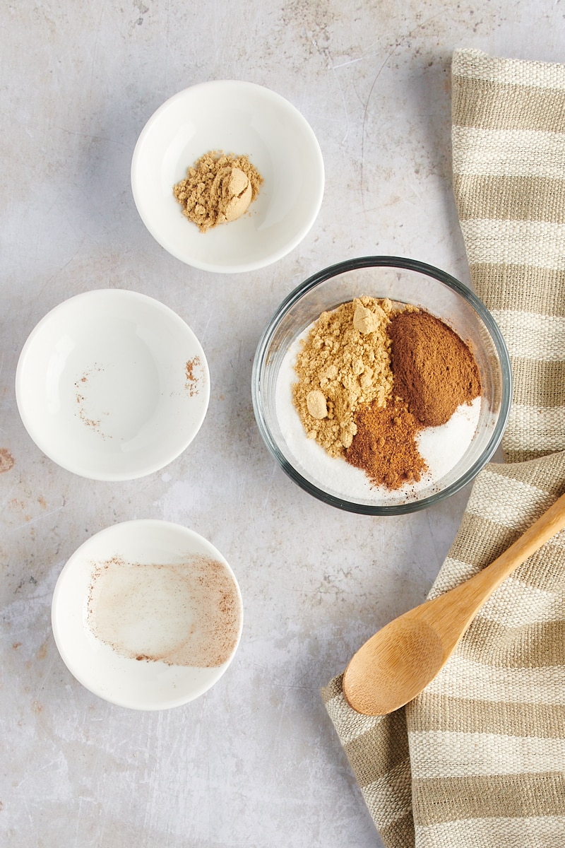 overhead view of sugar, ginger, cinnamon, and nutmeg in a glass mixing bowl