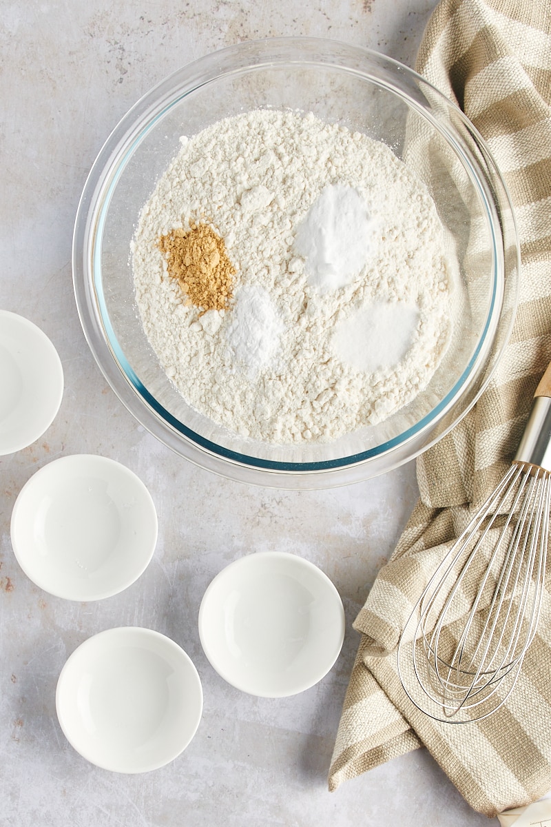 overhead view of flour, baking soda, ginger, cream of tartar, and salt in a glass mixing bowl