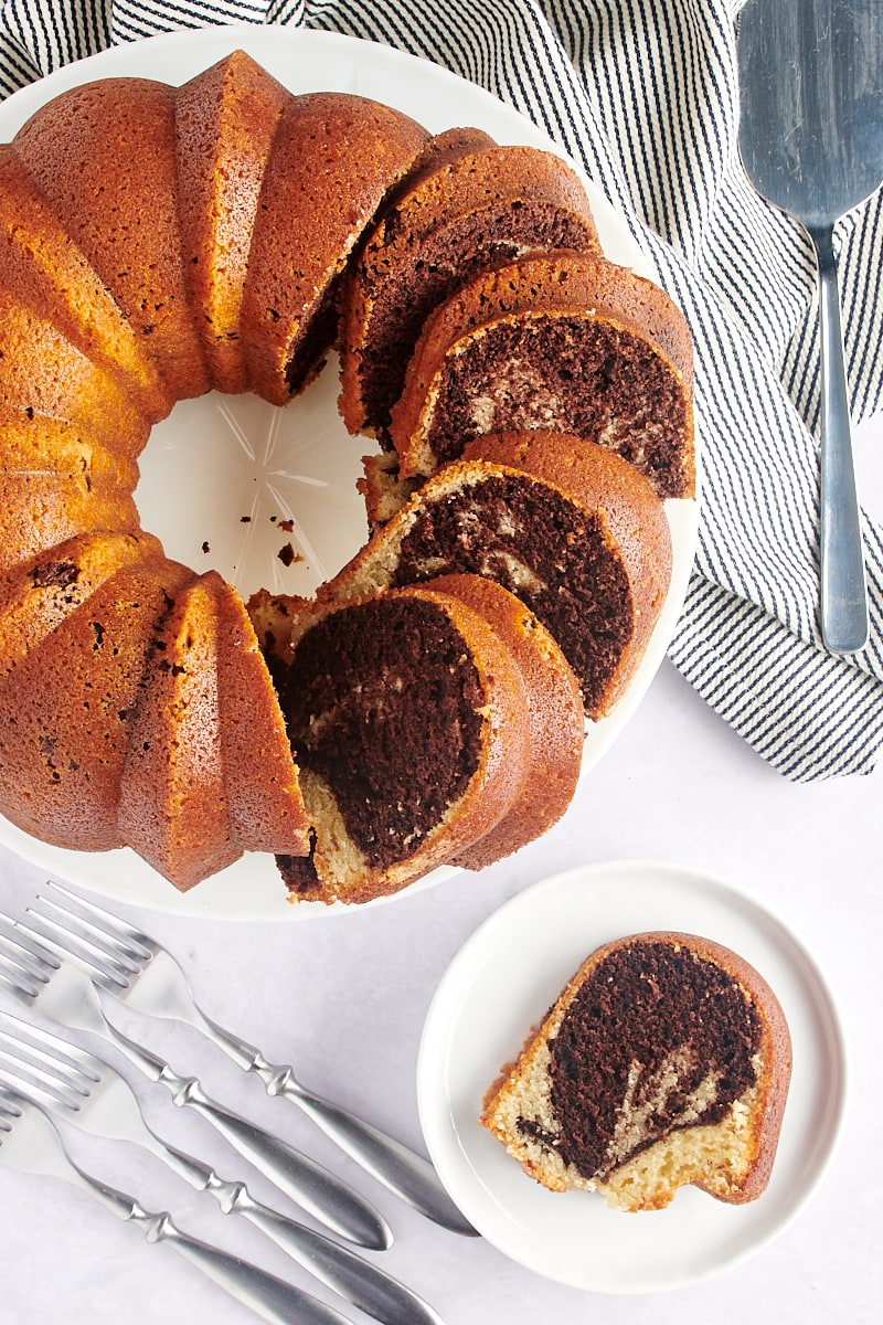 partially sliced Marble Bundt Cake on a white cake stand with a slice on a white plate next to it