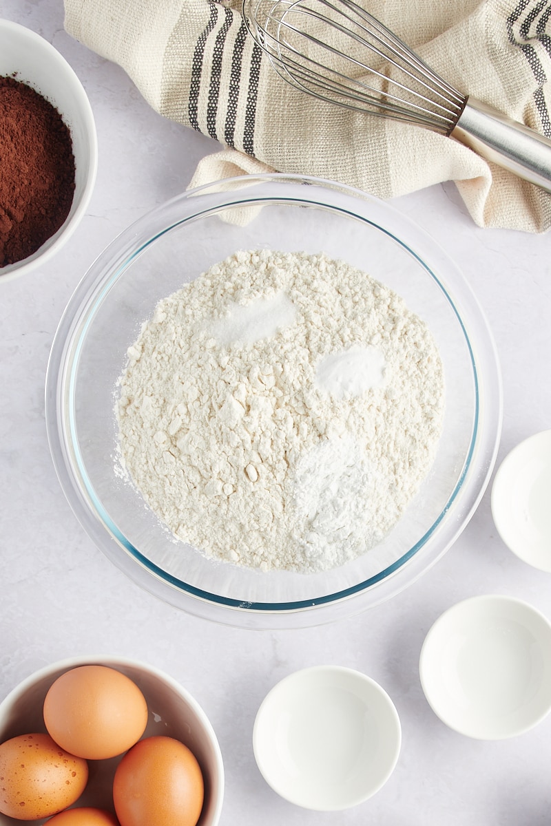 overhead view of flour, baking powder, baking soda, and salt in a glass mixing bowl