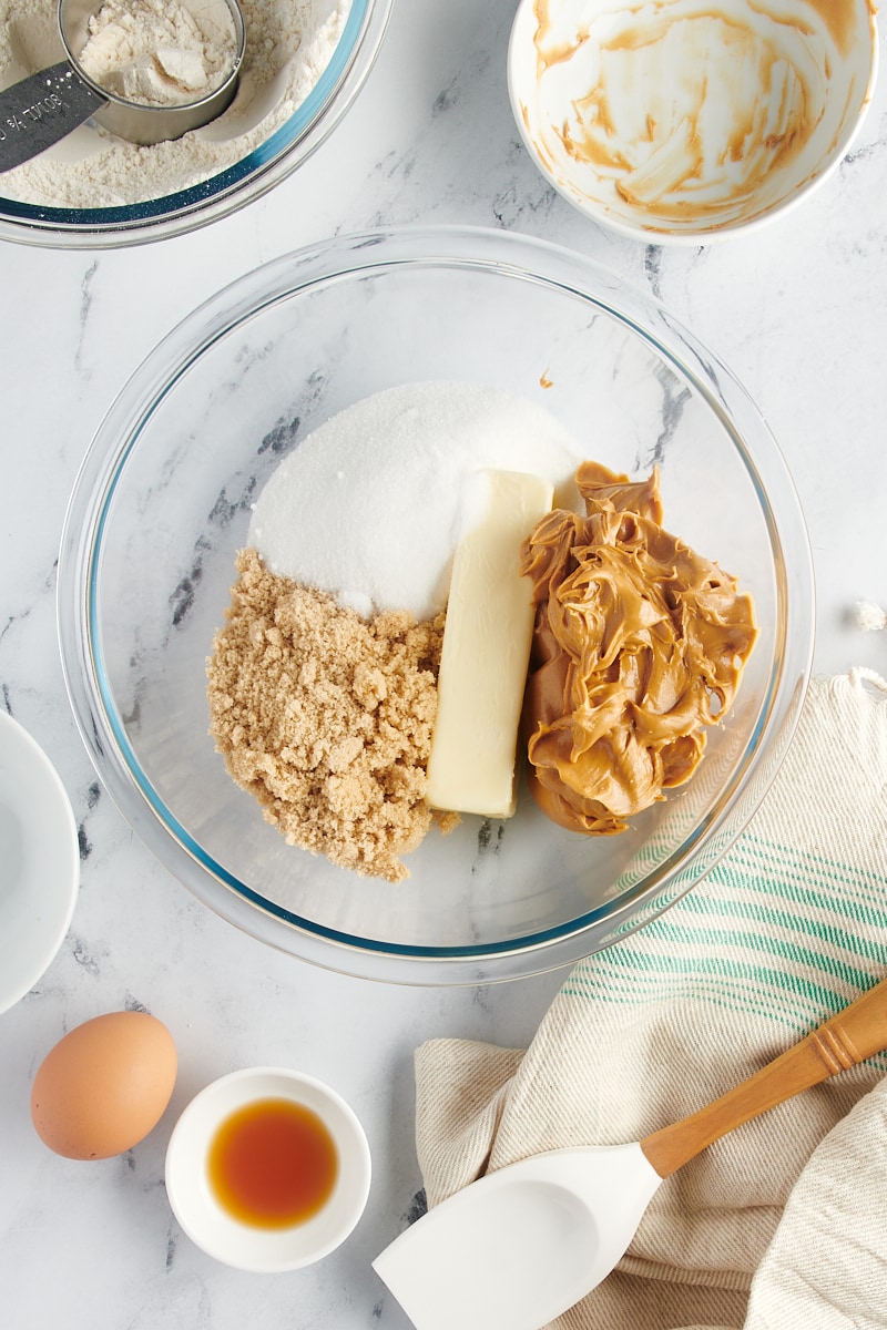 overhead view of butter, brown sugar, sugar, and peanut butter in a glass mixing bowl