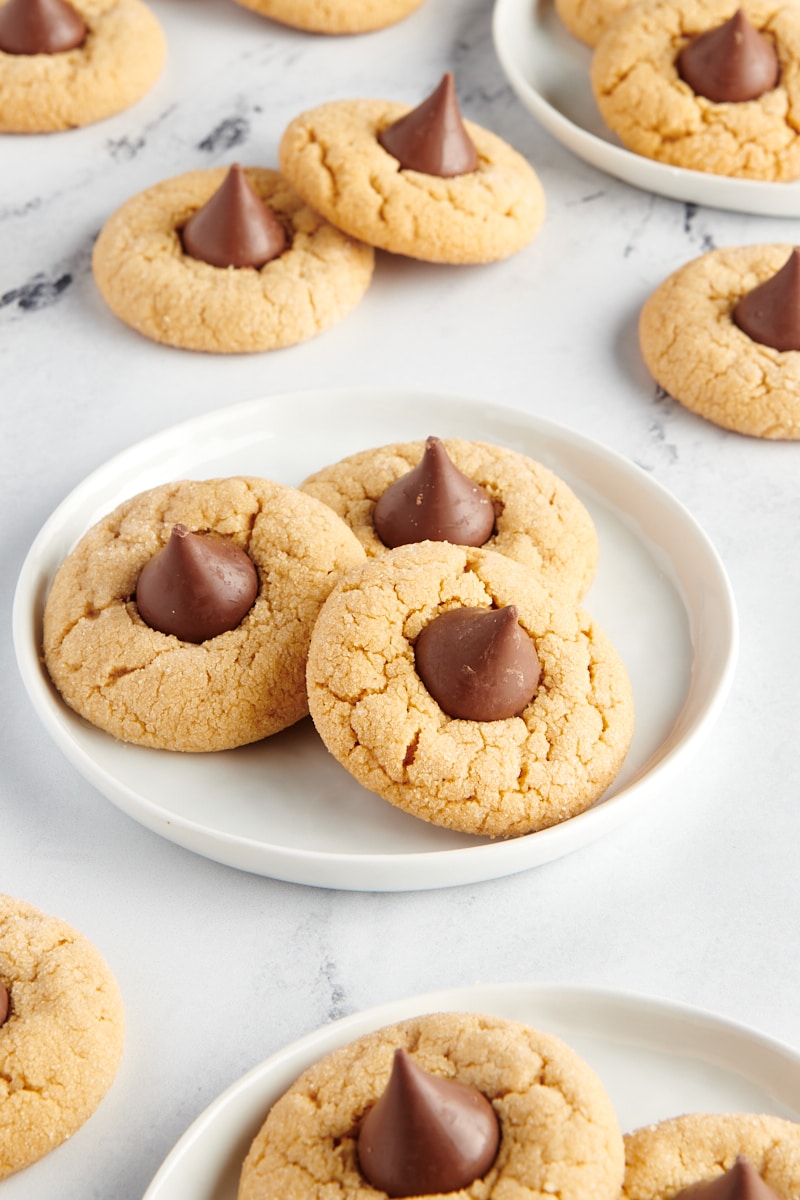 three Peanut Butter Blossoms on a white plate with more cookies surrounding
