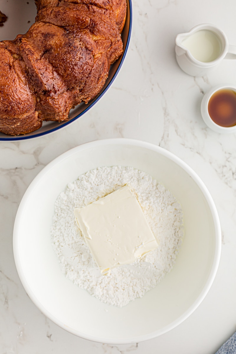 overhead view of cream cheese and confectioners' sugar in a white mixing bowl