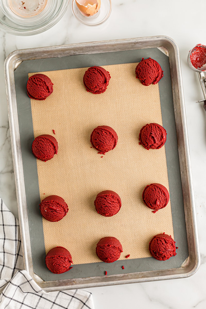 overhead view of portioned Red Velvet Cookie dough on a baking sheet lined with a silicone mat