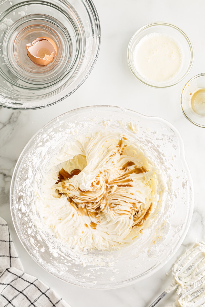 overhead view of vanilla extract added to cream cheese frosting in a glass mixing bowl