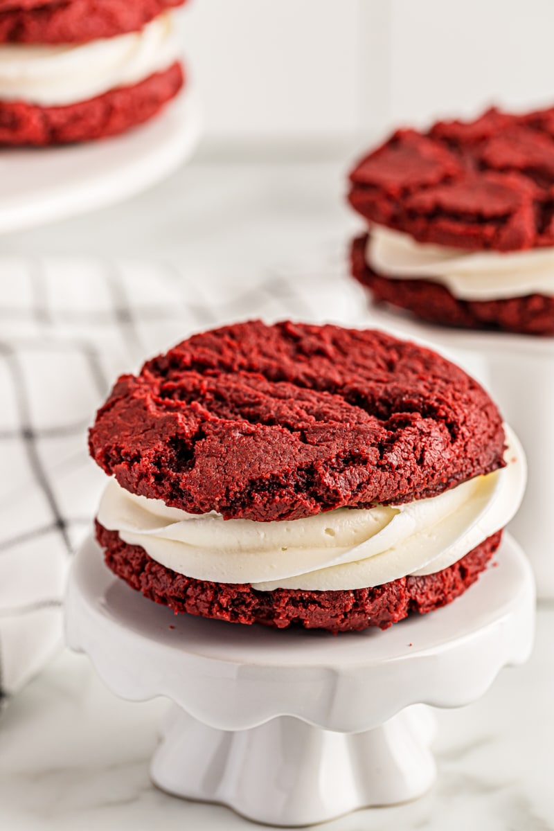 a Red Velvet Cookie on a small white pedestal with more cookies in the background