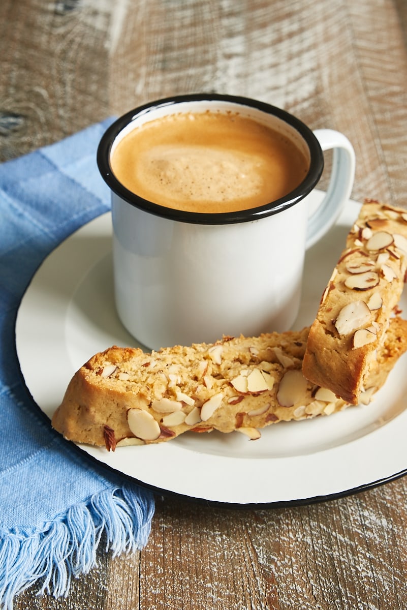 two Almond Biscotti on a white plate with a mug of coffee