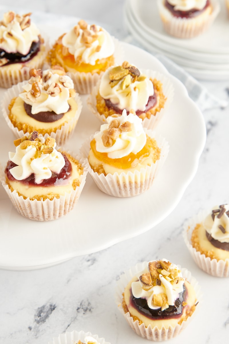 Mini cheesecakes on a cake stand and marble countertop.