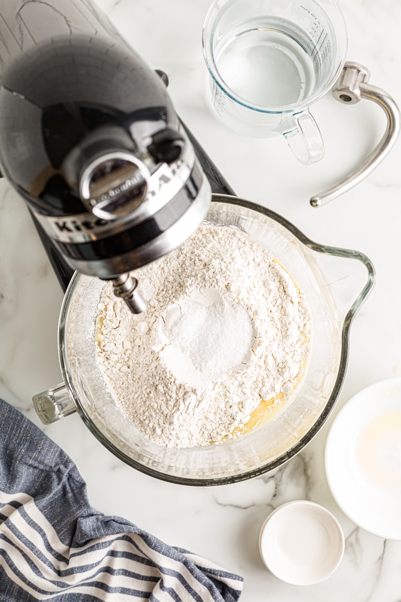overhead view of flour, yeast, sugar, salt, and water in the bowl of a stand mixer