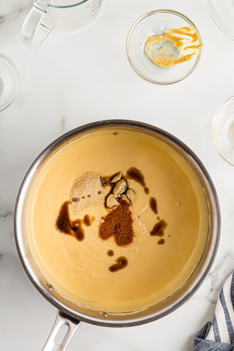 overhead view of mustard, Worcestershire, paprika, and garlic added to beer cheese dip in a saucepan