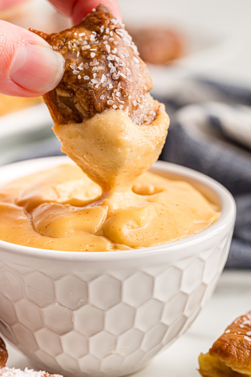 a pretzel bite being dipped into beer cheese dip