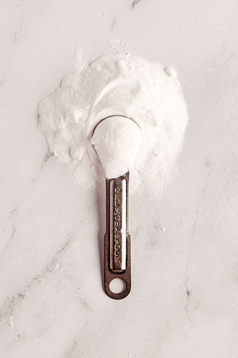 baking soda in a measuring spoon and in a pile on a marble surface