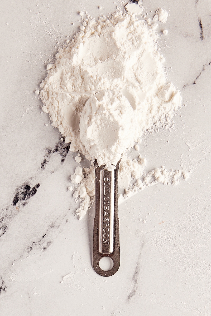overhead view of baking powder in a measuring spoon and in a pile on a marble surface