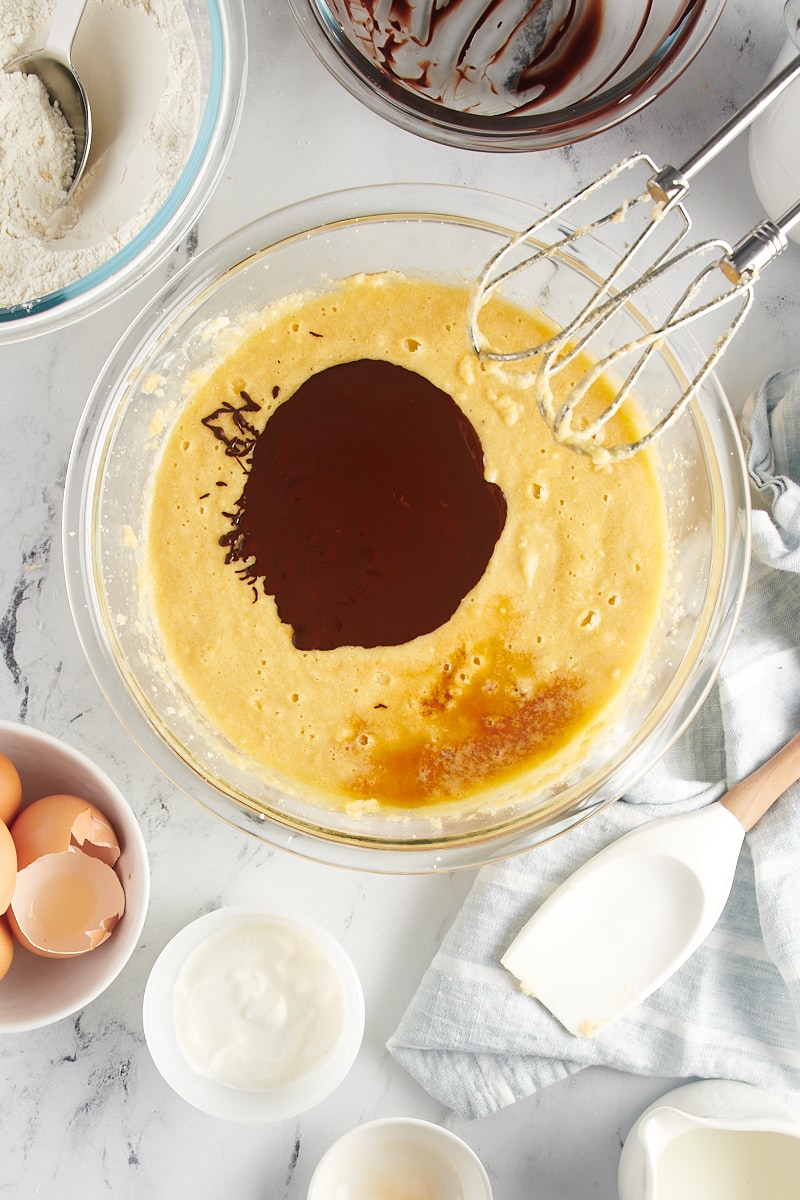 overhead view of melted chocolate and vanilla extract added to cake batter in a glass mixing bowl