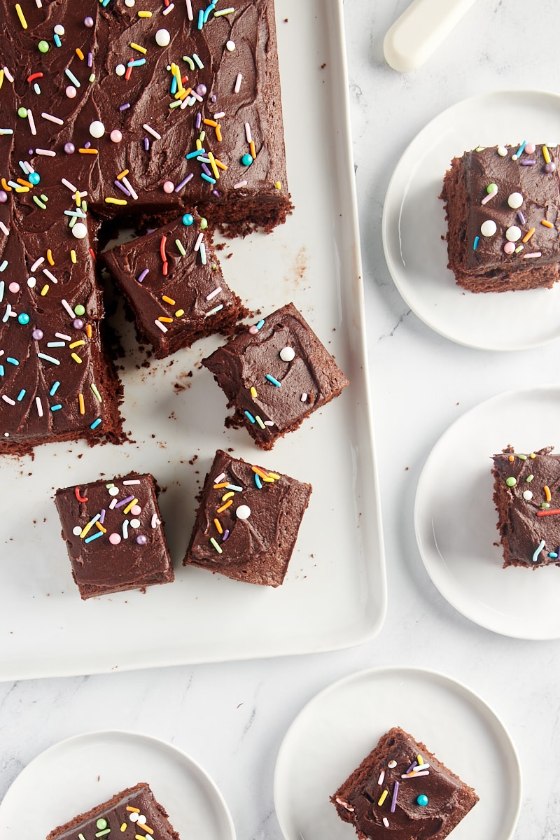 overhead view of partially sliced Chocolate Sheet Cake on a serving tray and on white plates