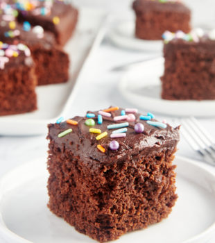 slice of Chocolate Sheet Cake on a white plate with more slices in the background