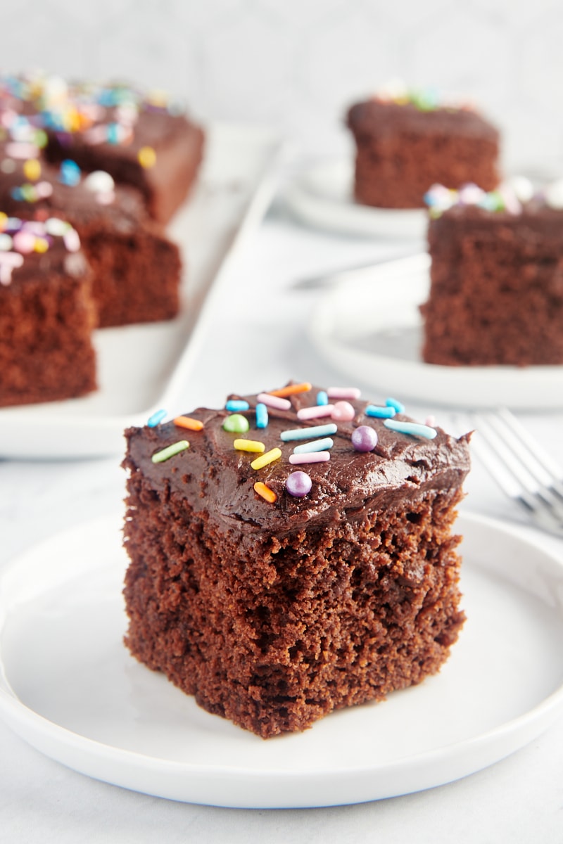 slice of Chocolate Sheet Cake on a white plate with more slices in the background