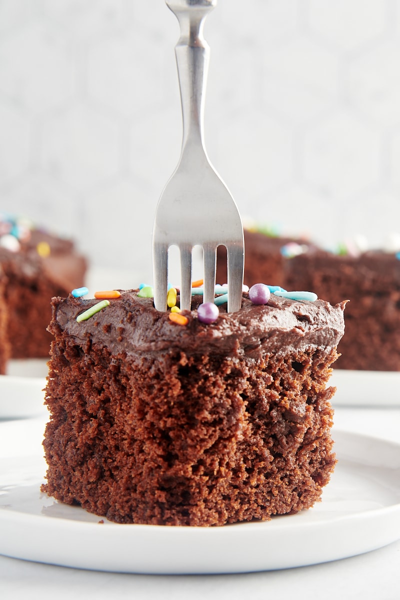 a fork cutting into a slice of Chocolate Sheet Cake on a white plate