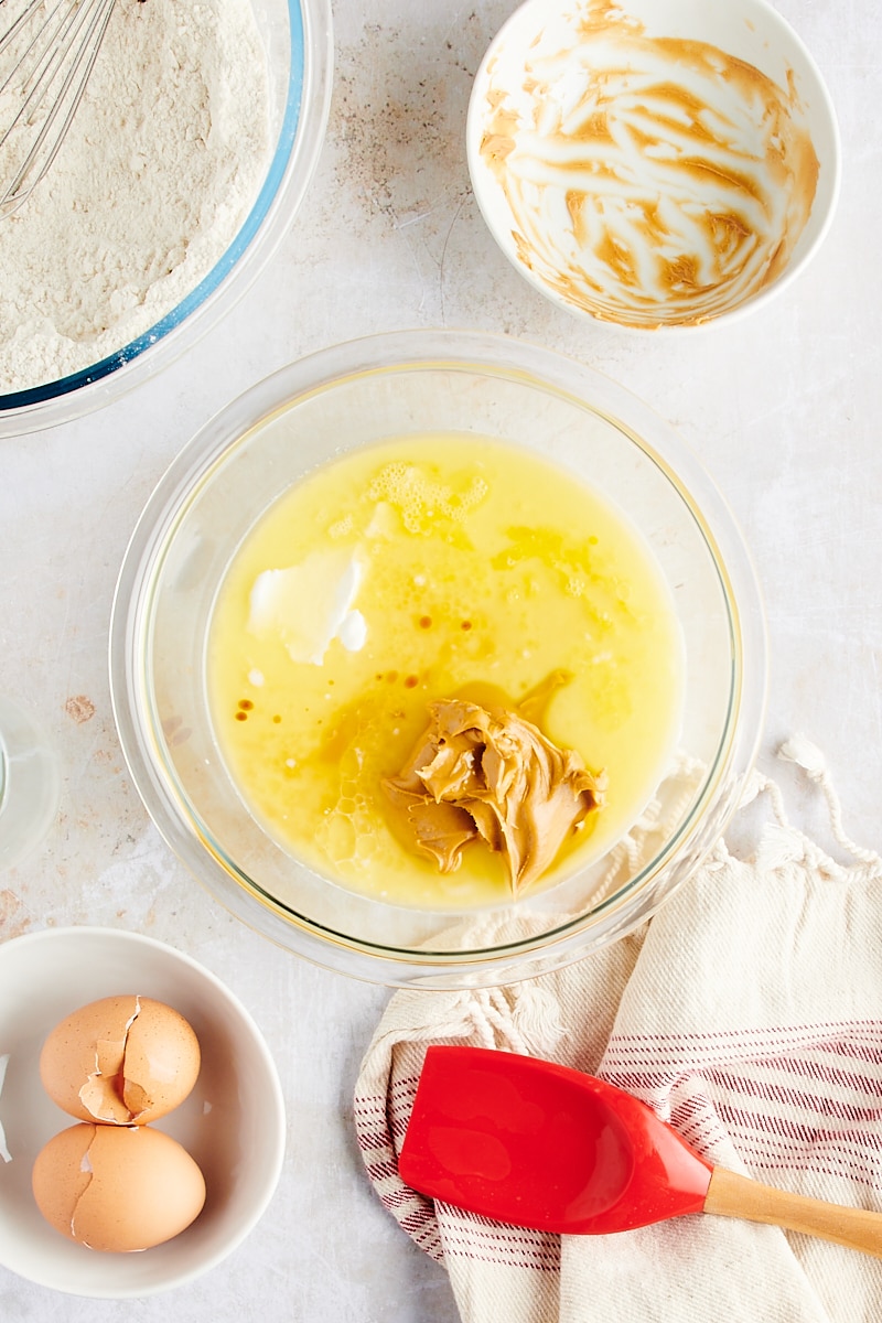 overhead view of butter, peanut butter, milk, sour cream, eggs, and vanilla in a glass mixing bowl