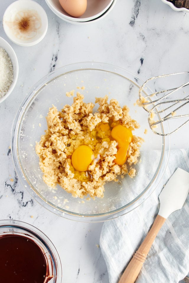 Overhead view of eggs cracked into bowl with creamed butter and sugar