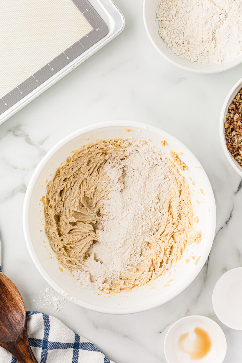 Overhead view of dry ingredients added to bowl of pecan sandies dough.