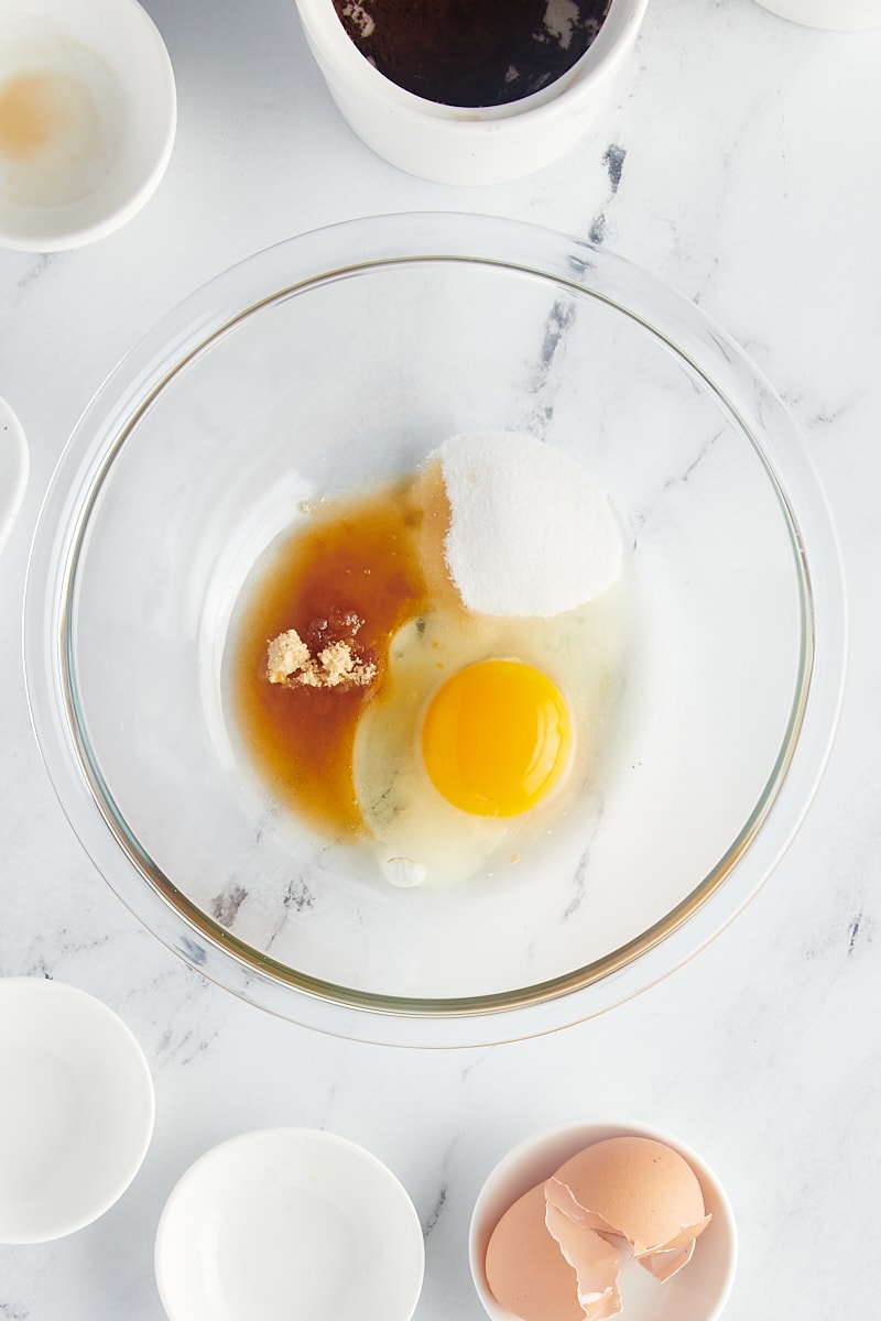 overhead view of sugar, brown sugar, egg, vanilla, and salt in a glass mixing bowl