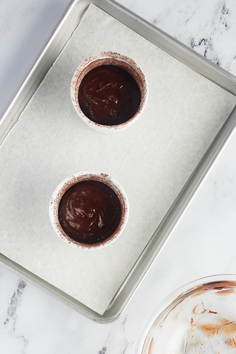 overhead view of flourless chocolate cake batter in ramekins on a lined quarter sheet pan