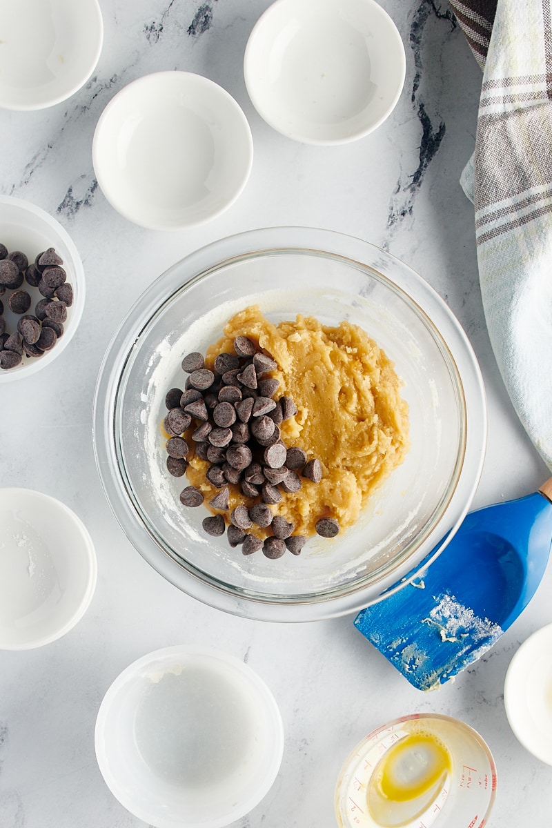 overhead view of chocolate chips added to cookie dough in a glass mixing bowl