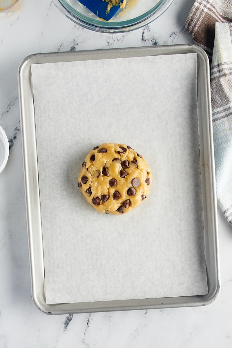 overhead view of giant chocolate chip cookie dough on a parchment-lined baking sheet ready to go into the oven